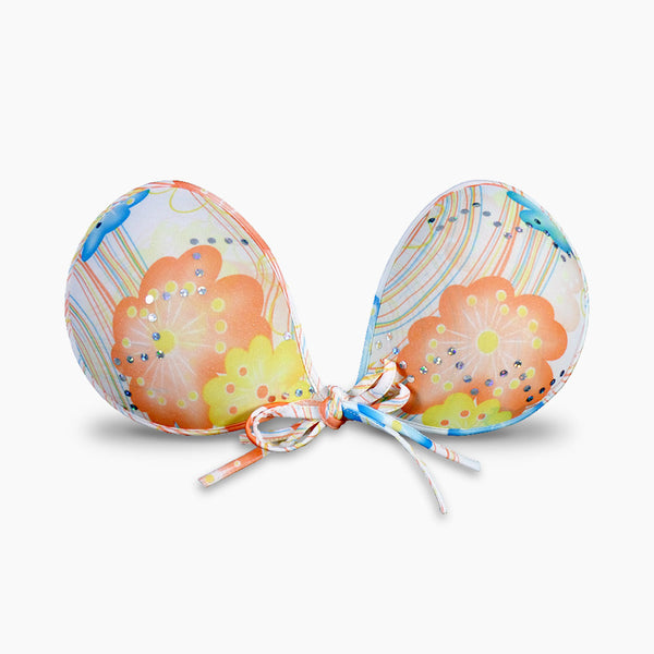 The Floral Tropics NuBra A100T 6TF27W is a bold strapless backless adhesive bra with a front tie instead of the traditional NuBra clasp. The bra has a white background with orange, yellow, and blue floral designs on it.